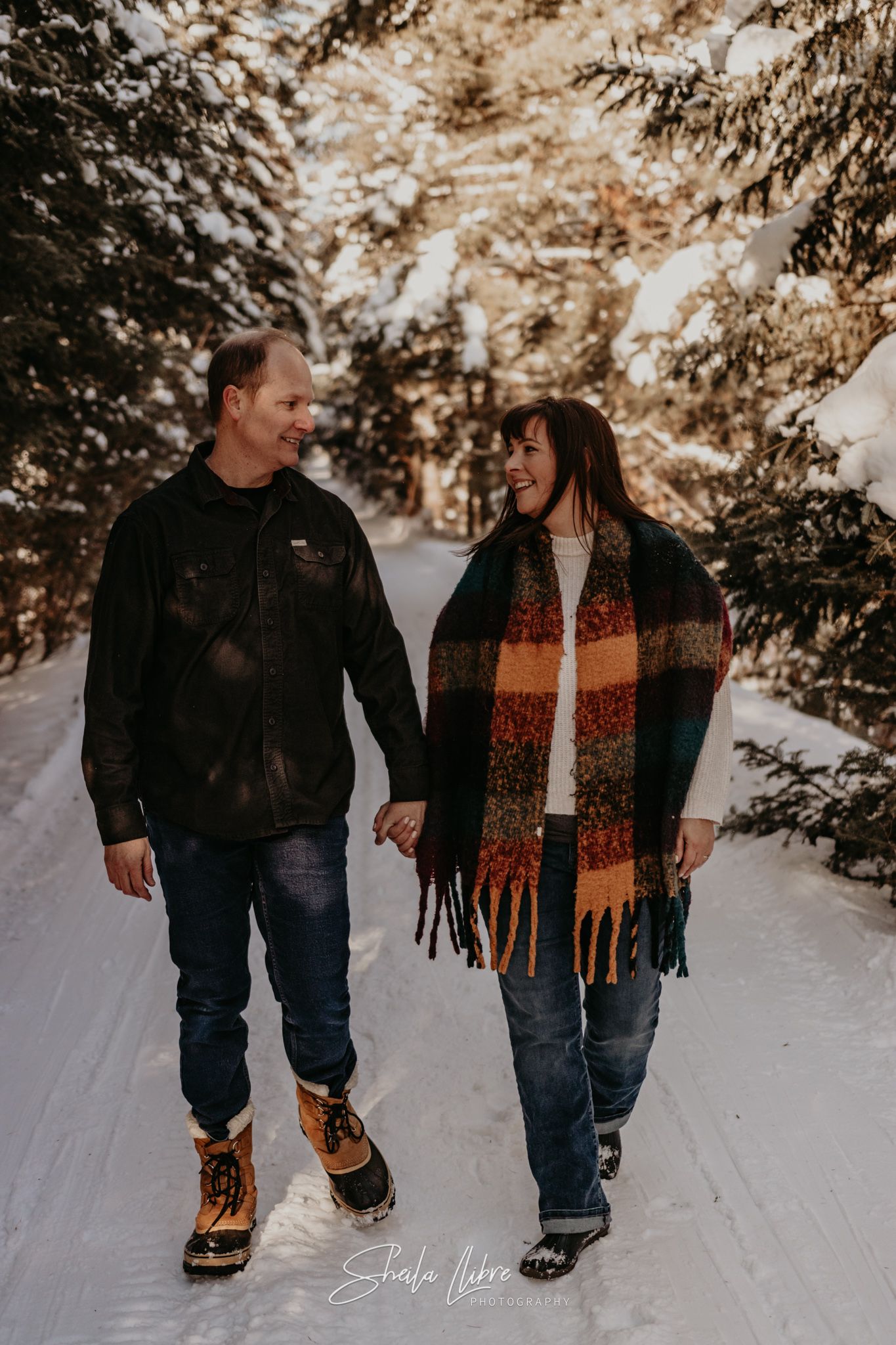 A couple takes a romantic winter walk together on a snow-covered forest trail.
