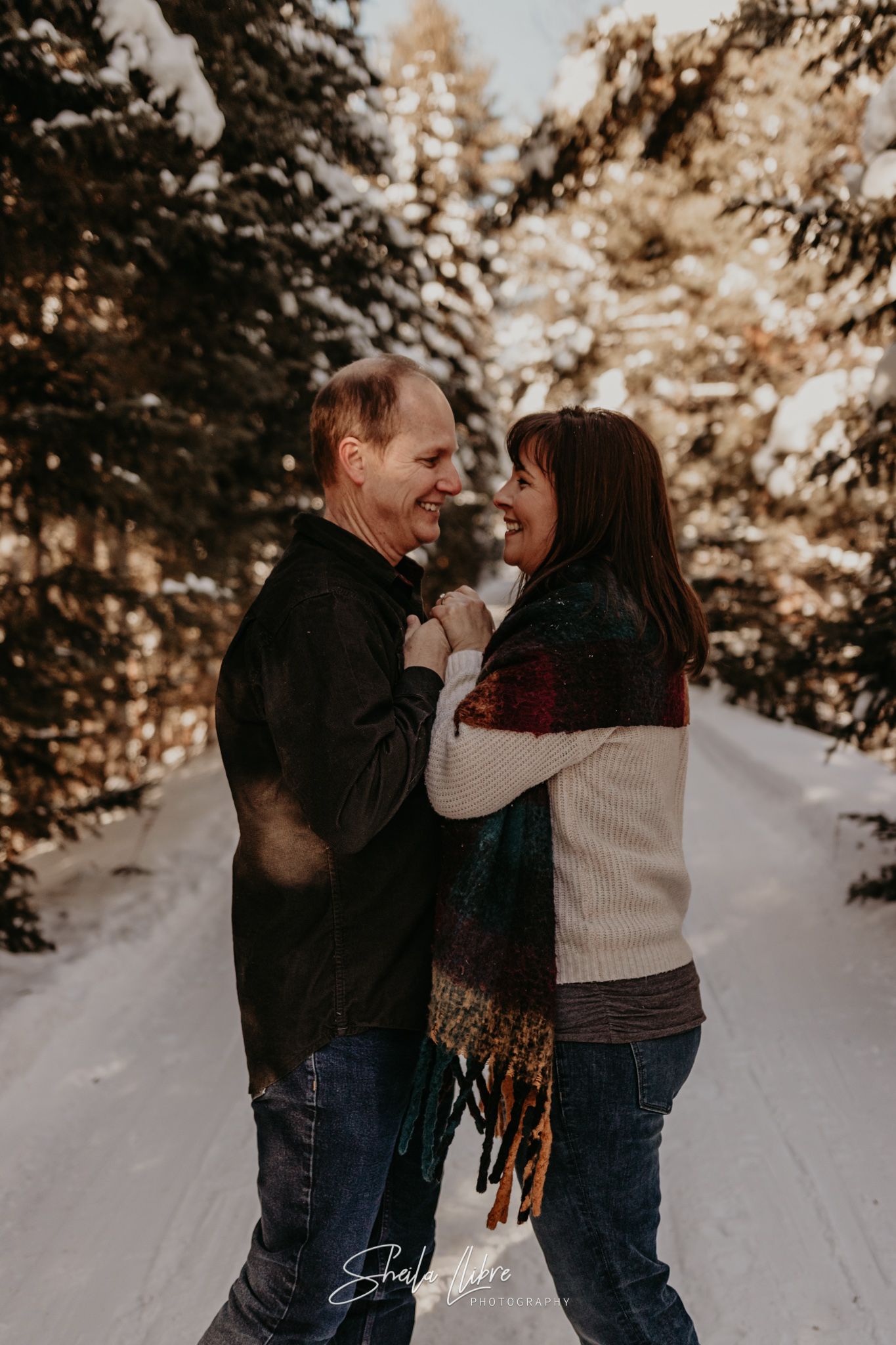 A joyful winter photoshoot showing a couple laughing together on a snowy forest path.