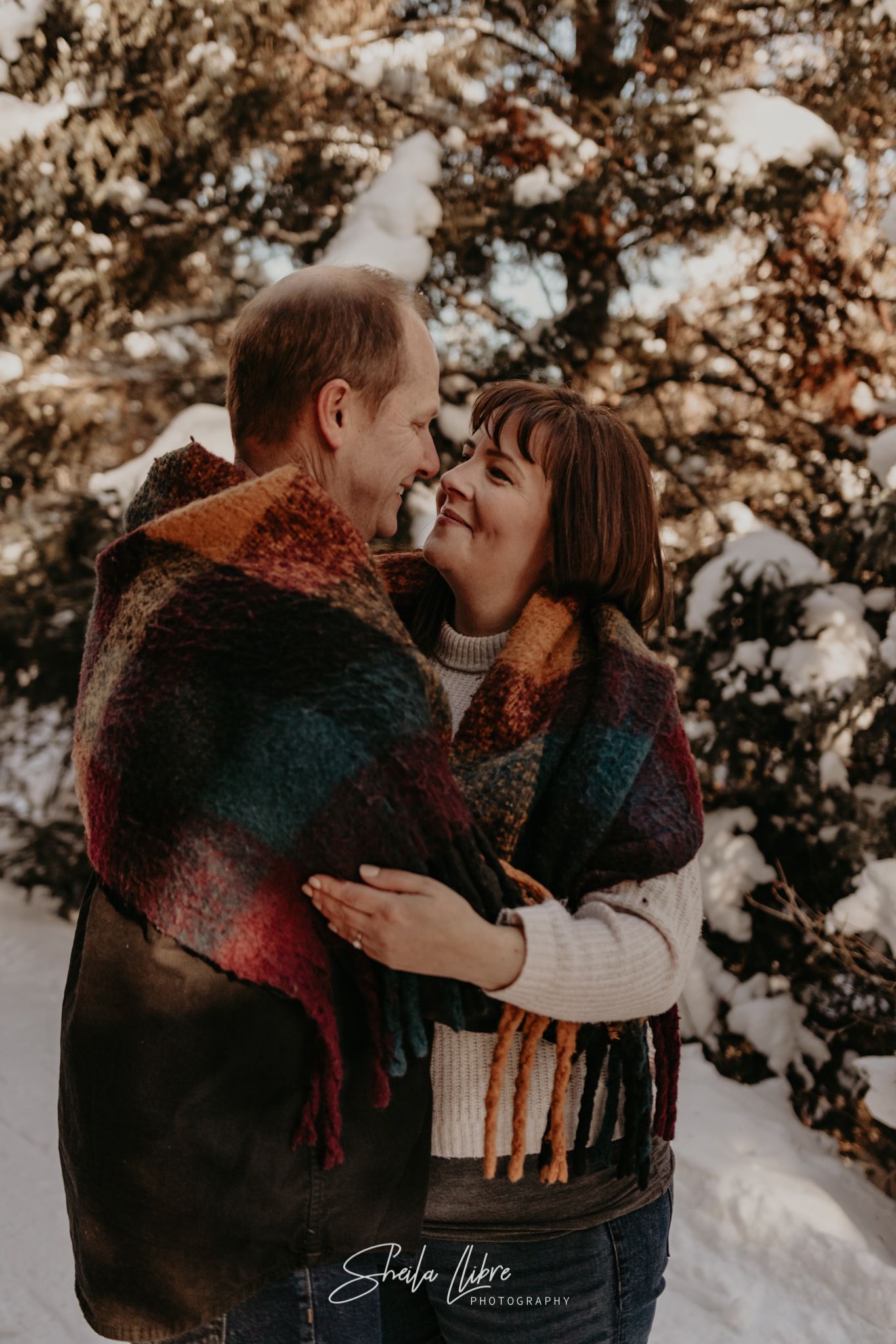 A romantic winter moment between a couple sharing a colorful plaid scarf in the snow.