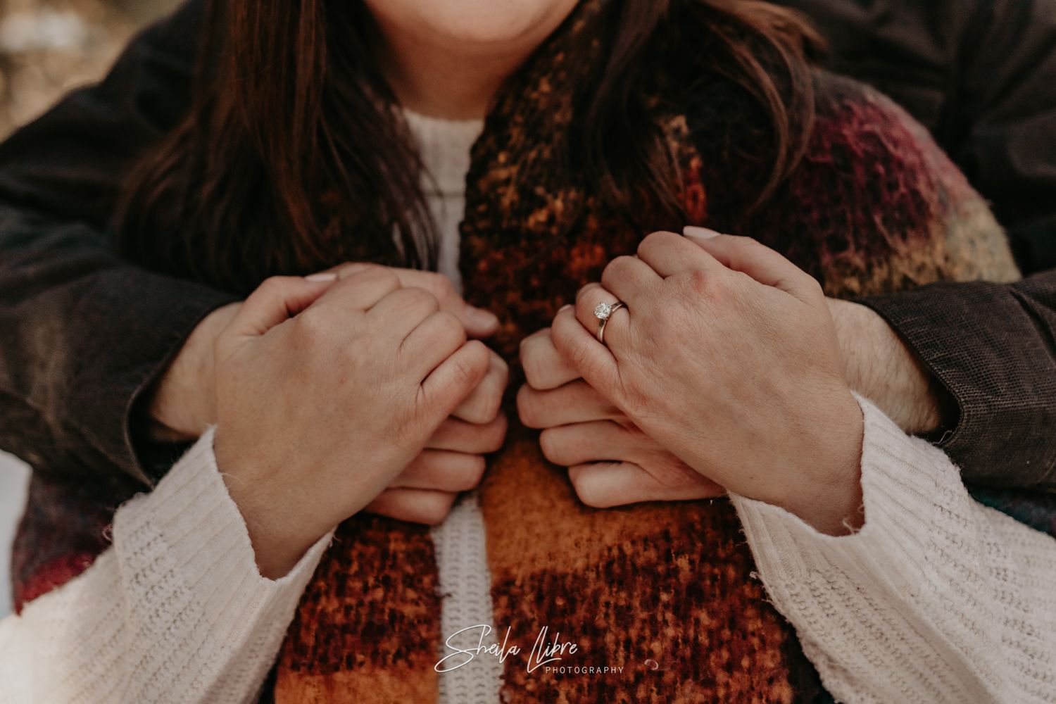 Close-up shot of hands clasped together wearing winter clothing against a snowy background.