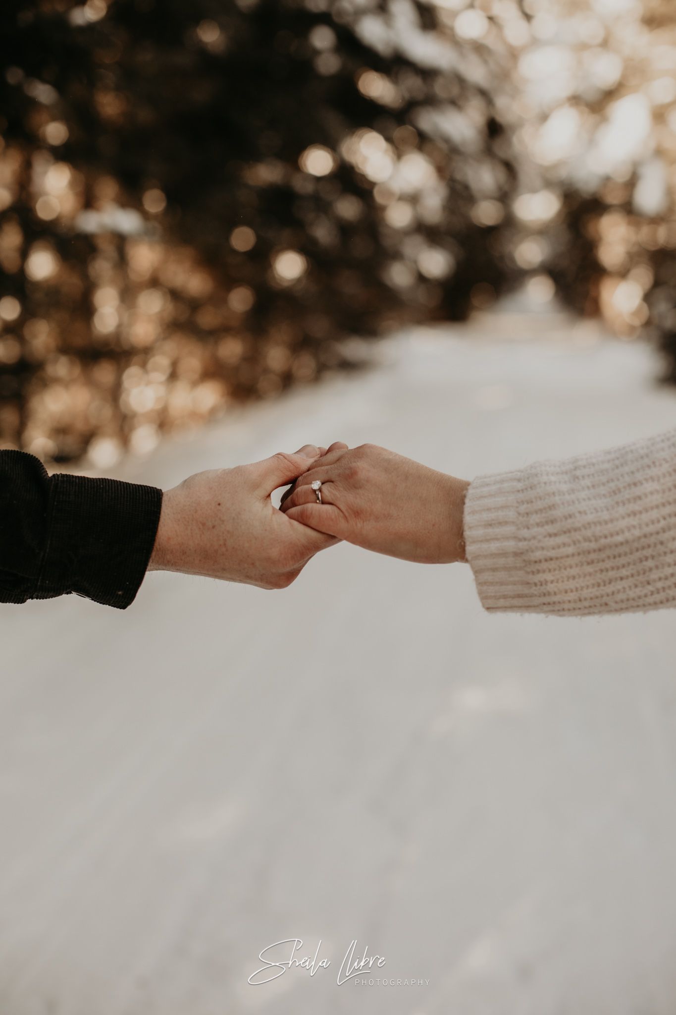 Close-up of hands touching with an engagement ring visible against a snowy winter backdrop.