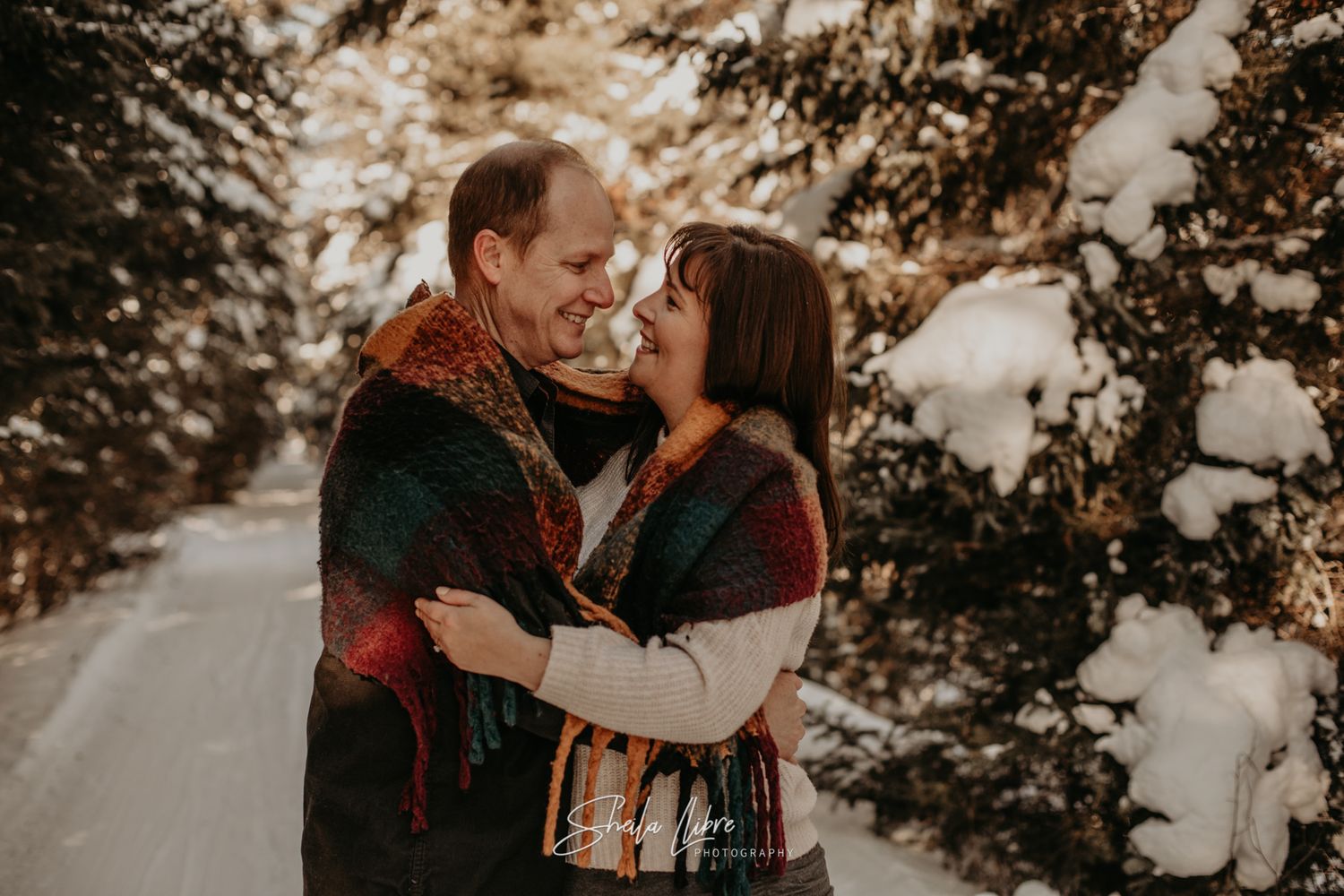 Romantic winter engagement photo of couple sharing intimate moment on snowy path.