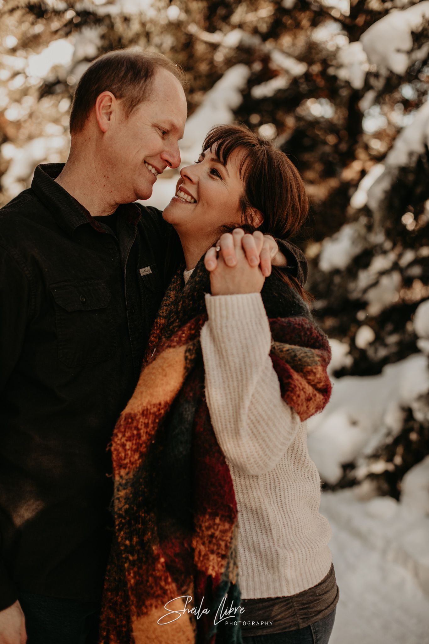 Joyful winter engagement photo of couple laughing together in the snow.