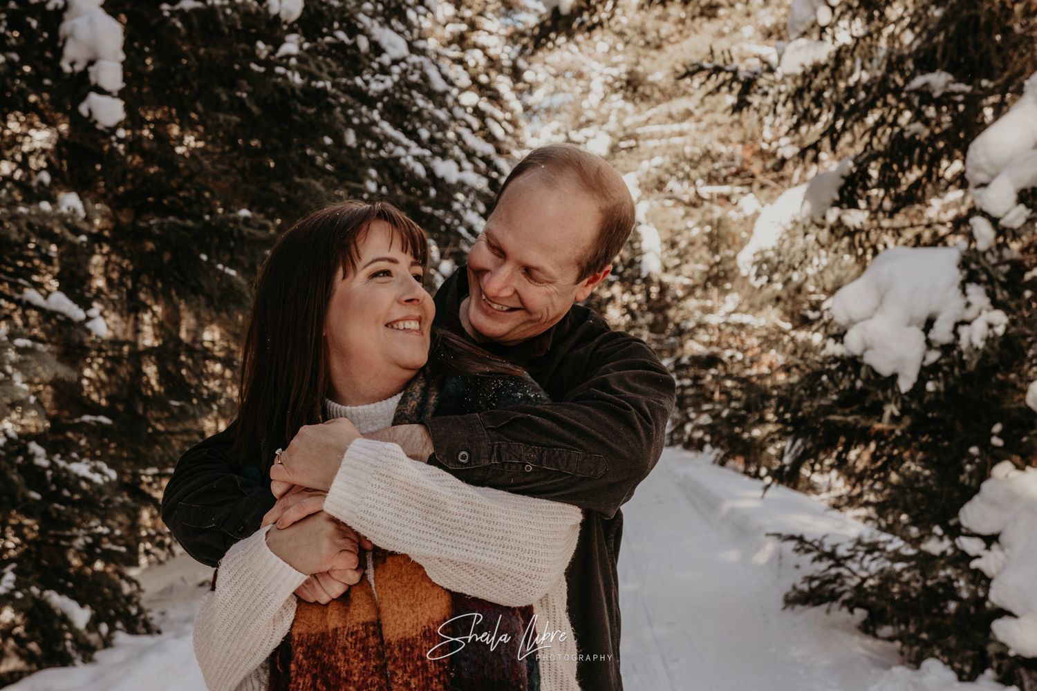 A couple embraces while sharing a warm moment in a snowy winter forest setting.