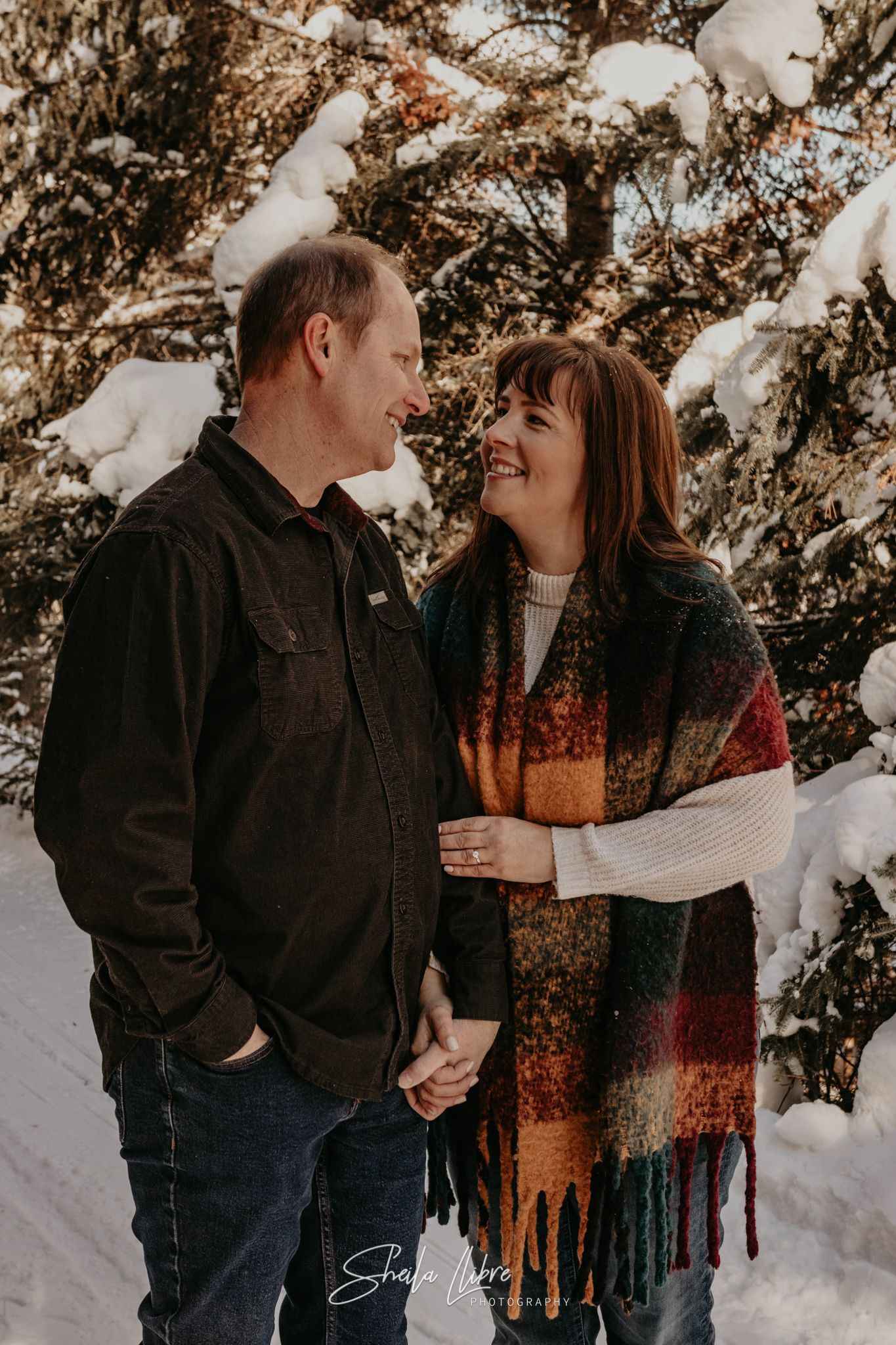 A couple shares an intimate moment while standing together in a snowy forest setting.