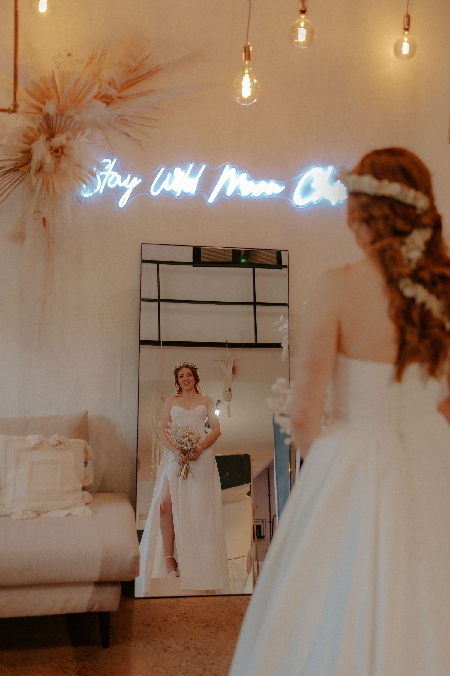 A bridal boutique interior with neon sign and mirror reflecting wedding dress displays.