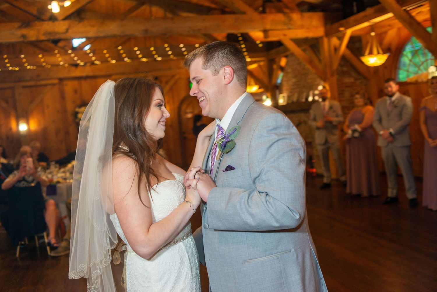 A tender moment between newlyweds dancing in a warmly lit rustic reception venue.