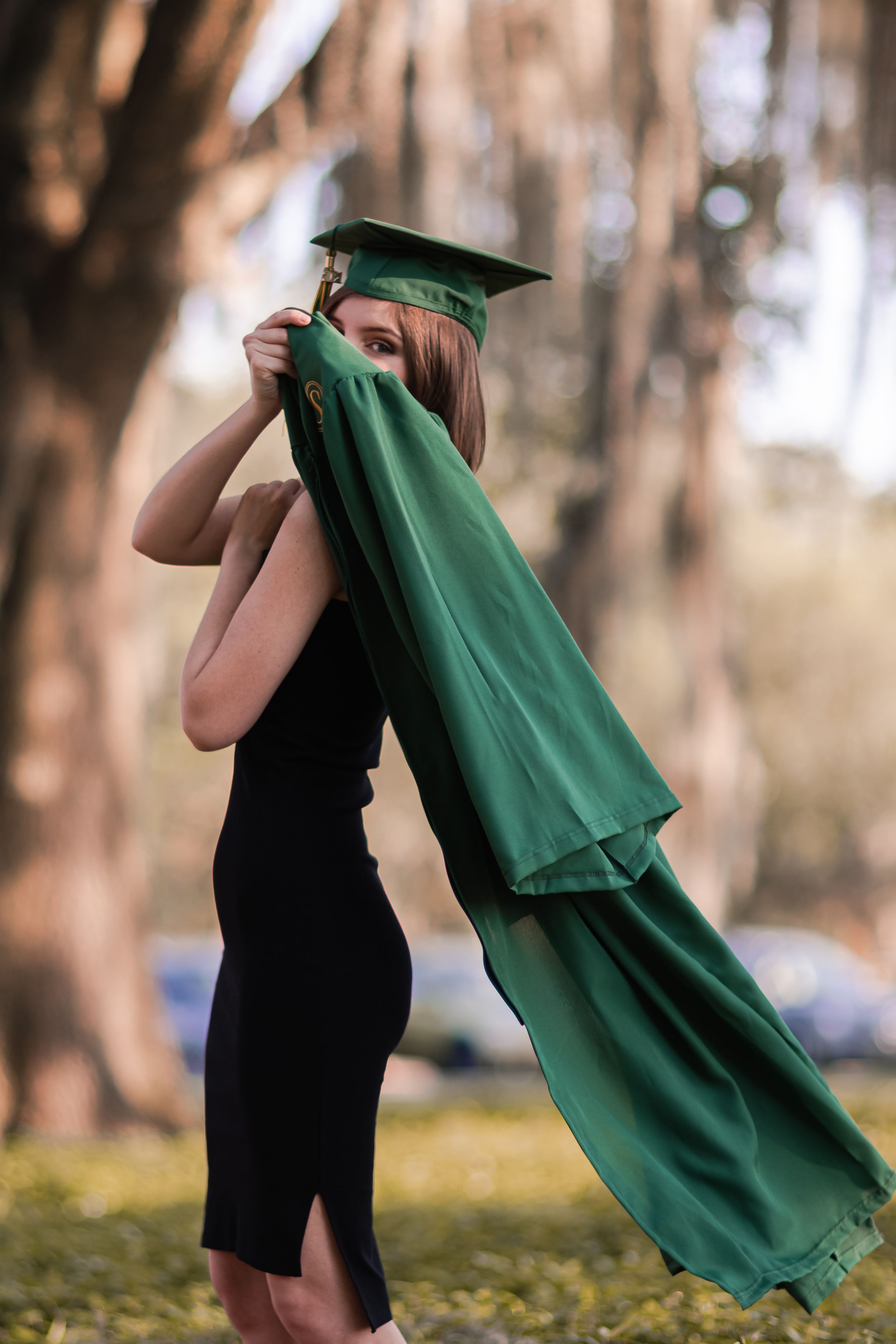 Graduate playing with green graduation gown during outdoor photo session.