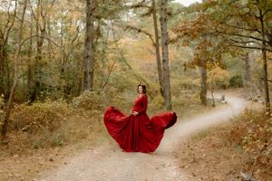 A flowing red dress creates drama on a wooded path during a maternity photo session.