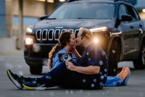 Couple sitting on ground in front of Jeep Cherokee with headlights creating romantic evening ambiance.