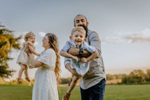 Joyful outdoor family scene with parents playing with children in a sunlit field.