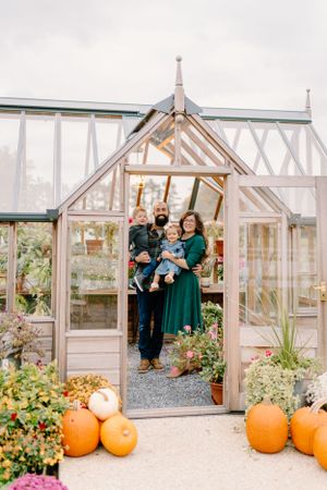 Family standing in a greenhouse doorway decorated with orange pumpkins for fall.