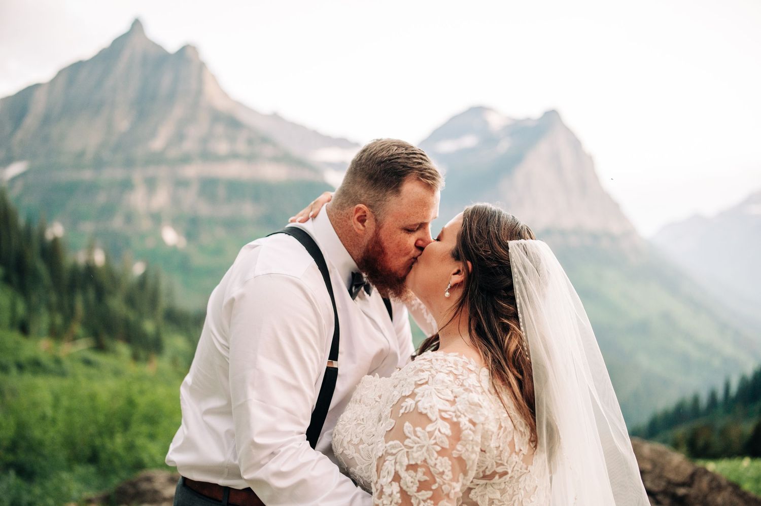 Couple kissing in wedding attire with mountains in the background