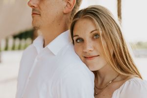A close-up portrait of a couple in white clothing against a light background.