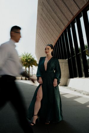 Fashion-forward couple poses dramatically under modern architecture with palm trees.