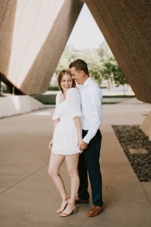 Sweet engagement portrait under geometric architecture in natural lighting.