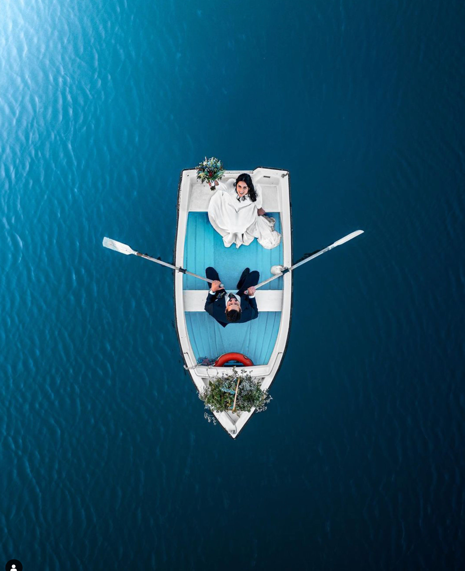 Aerial view of couple lying on white boat deck surrounded by deep blue ocean waters.