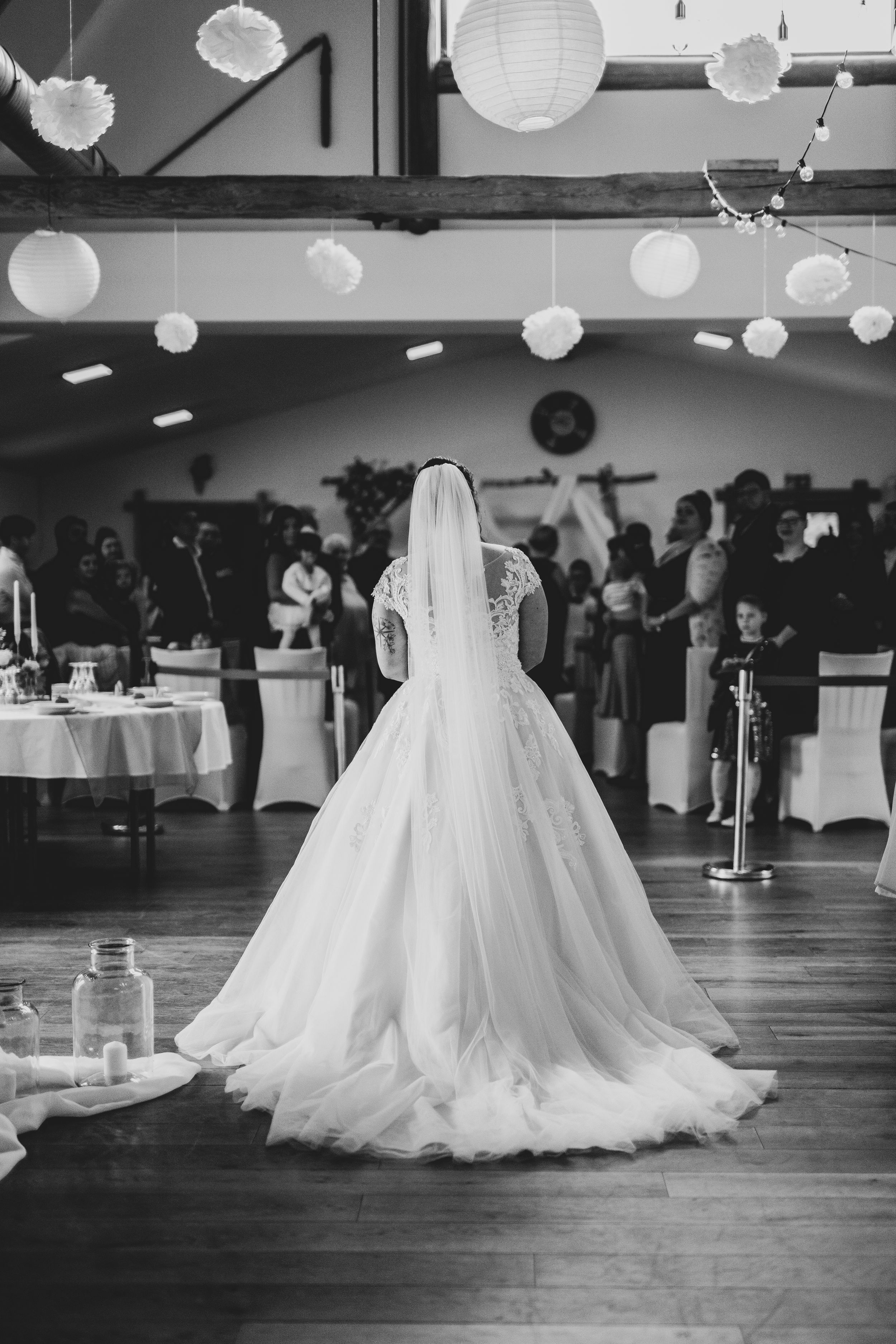 Bride in ballgown silhouette standing in reception hall decorated with paper lanterns.