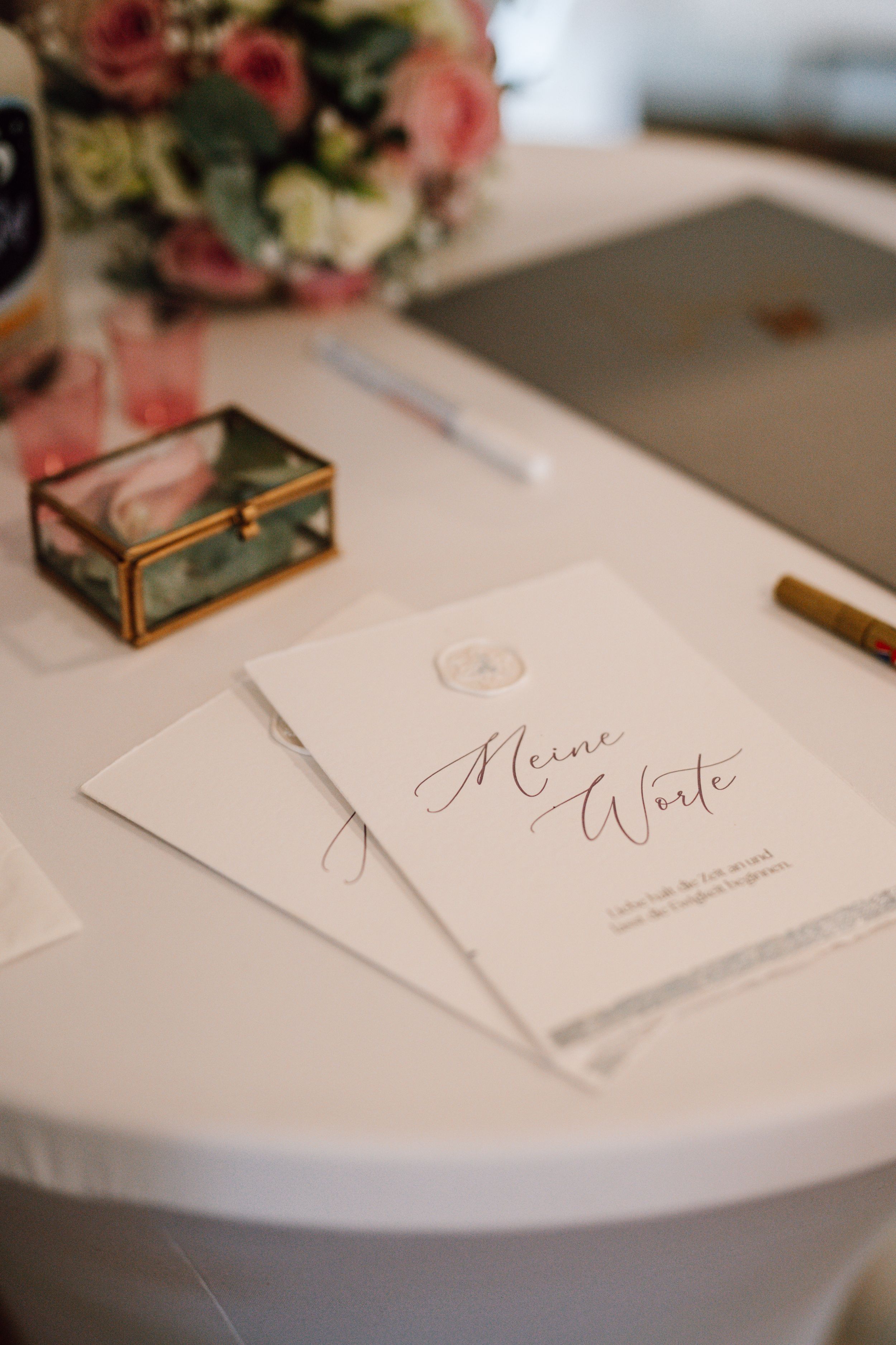 Wedding stationery with elegant calligraphy displayed on a white table with floral decorations.