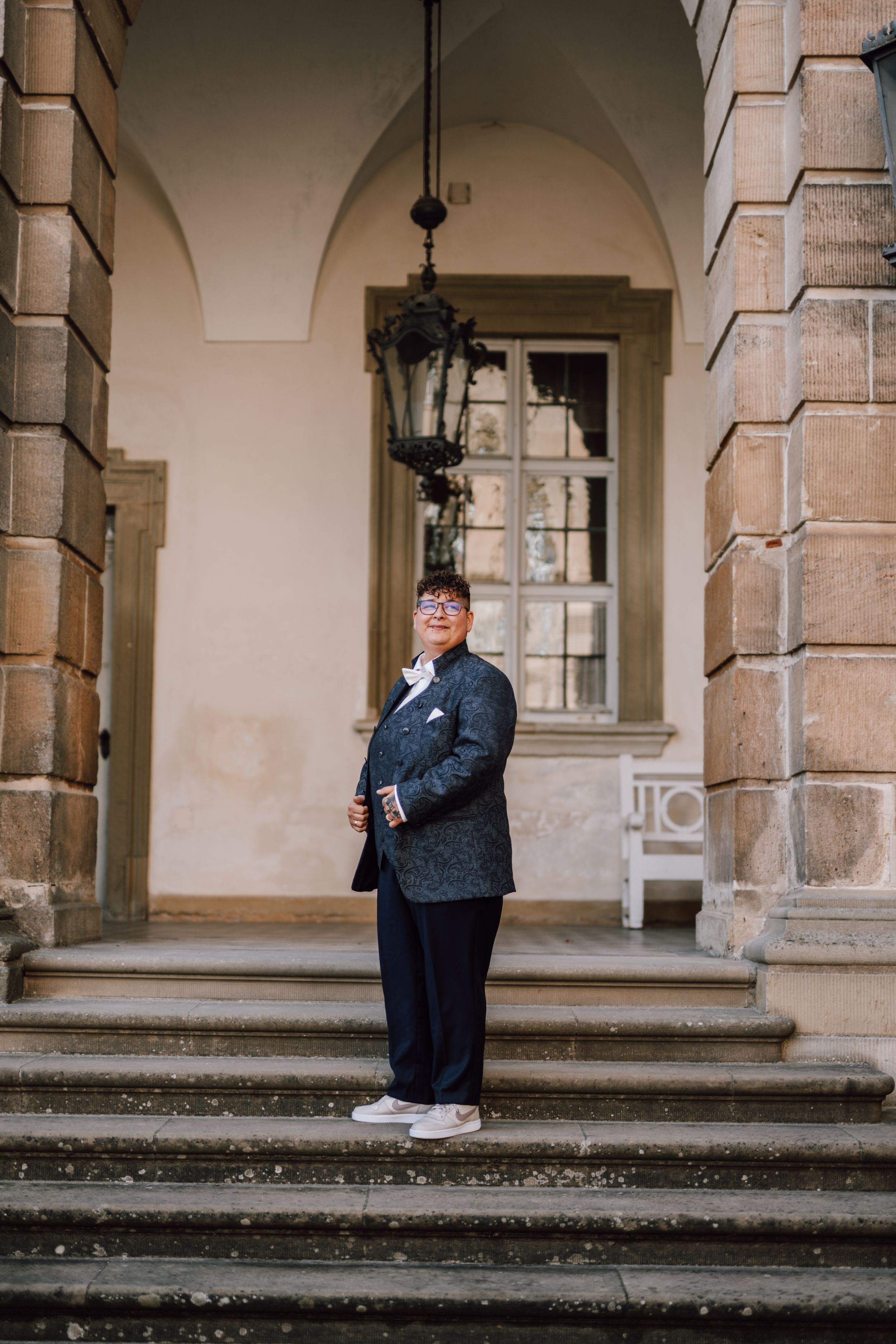 A formal portrait on stone steps with classical architectural elements and hanging lanterns.