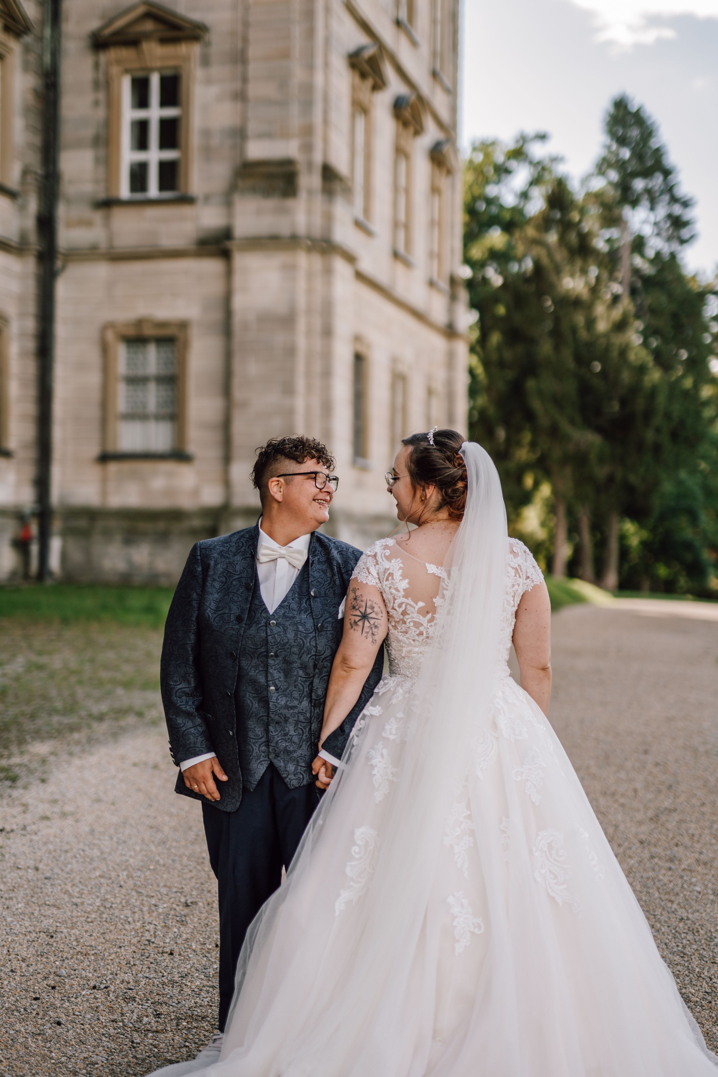 A wedding couple shares a tender moment on a gravel path by a historic stone building.