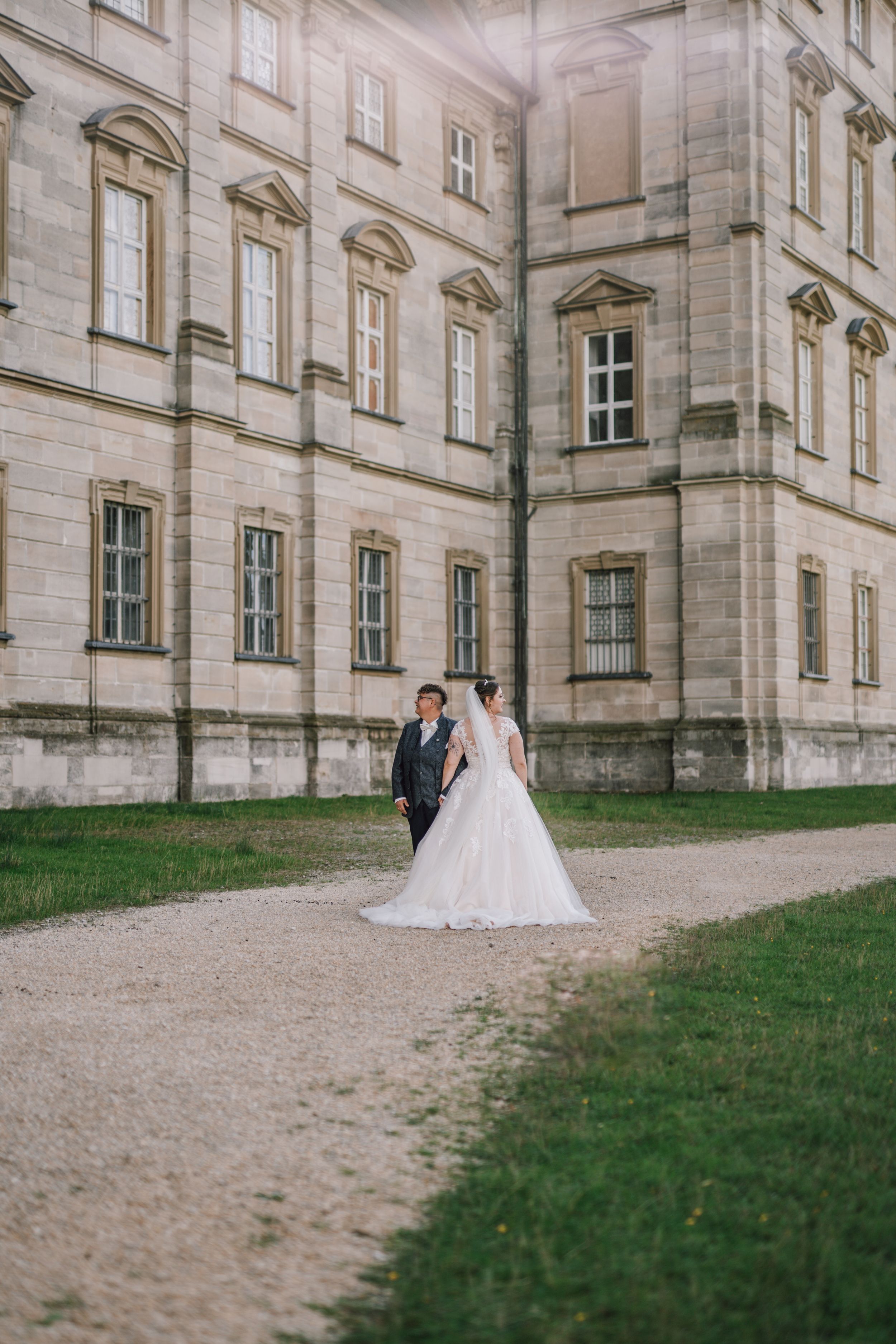 A wedding couple poses for photos outside a grand stone building with classical architecture.