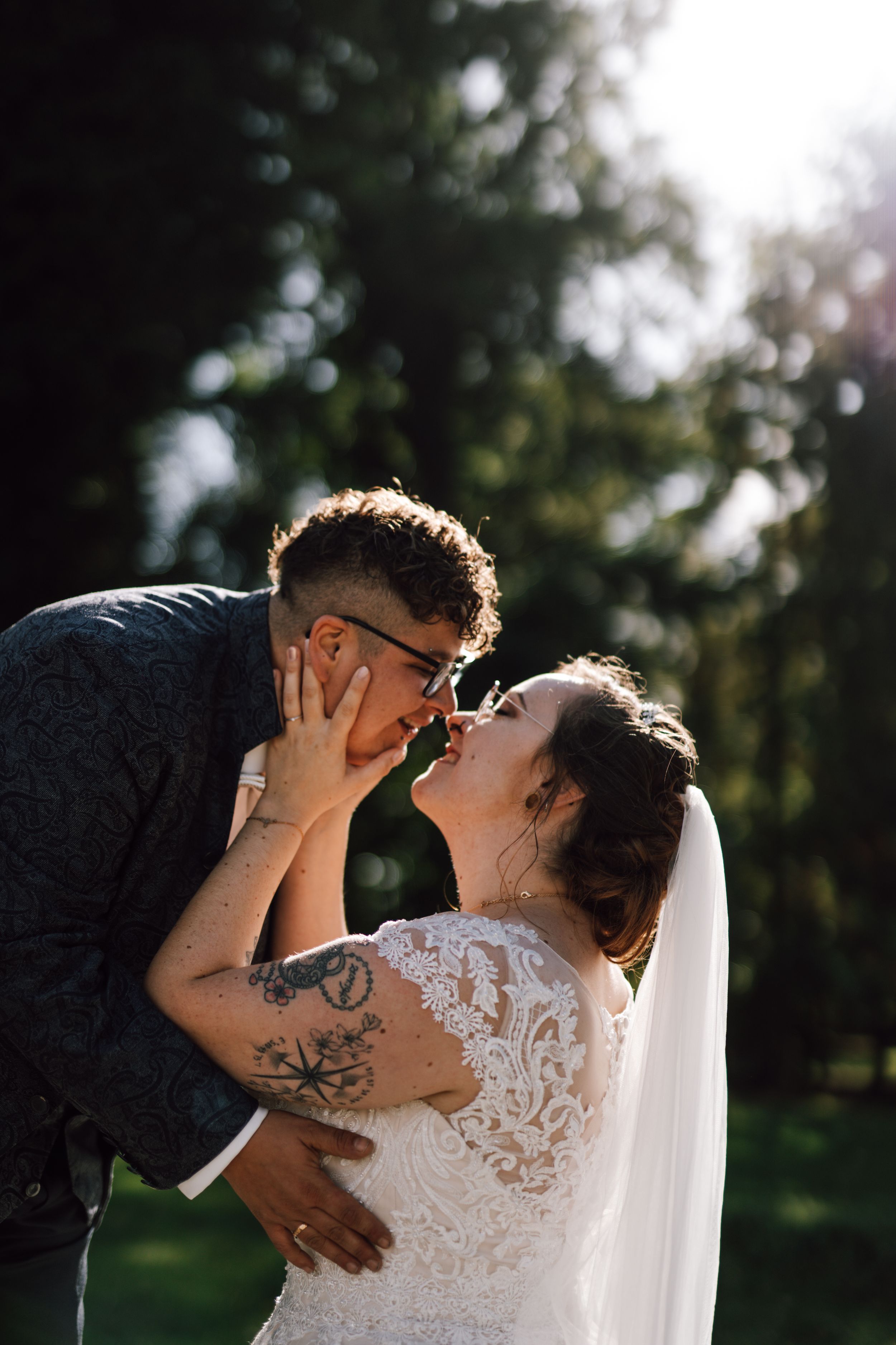 An intimate wedding moment captured in backlit natural outdoor setting.
