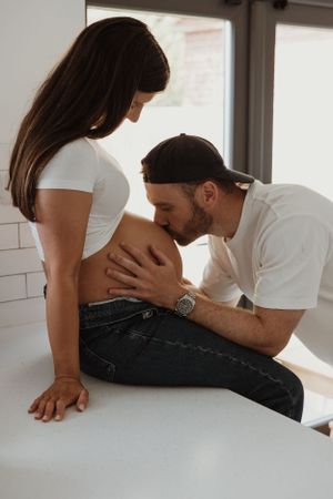 Pregnant lady and partner kissing baby bump photographed by Jennifer Thwaites photography