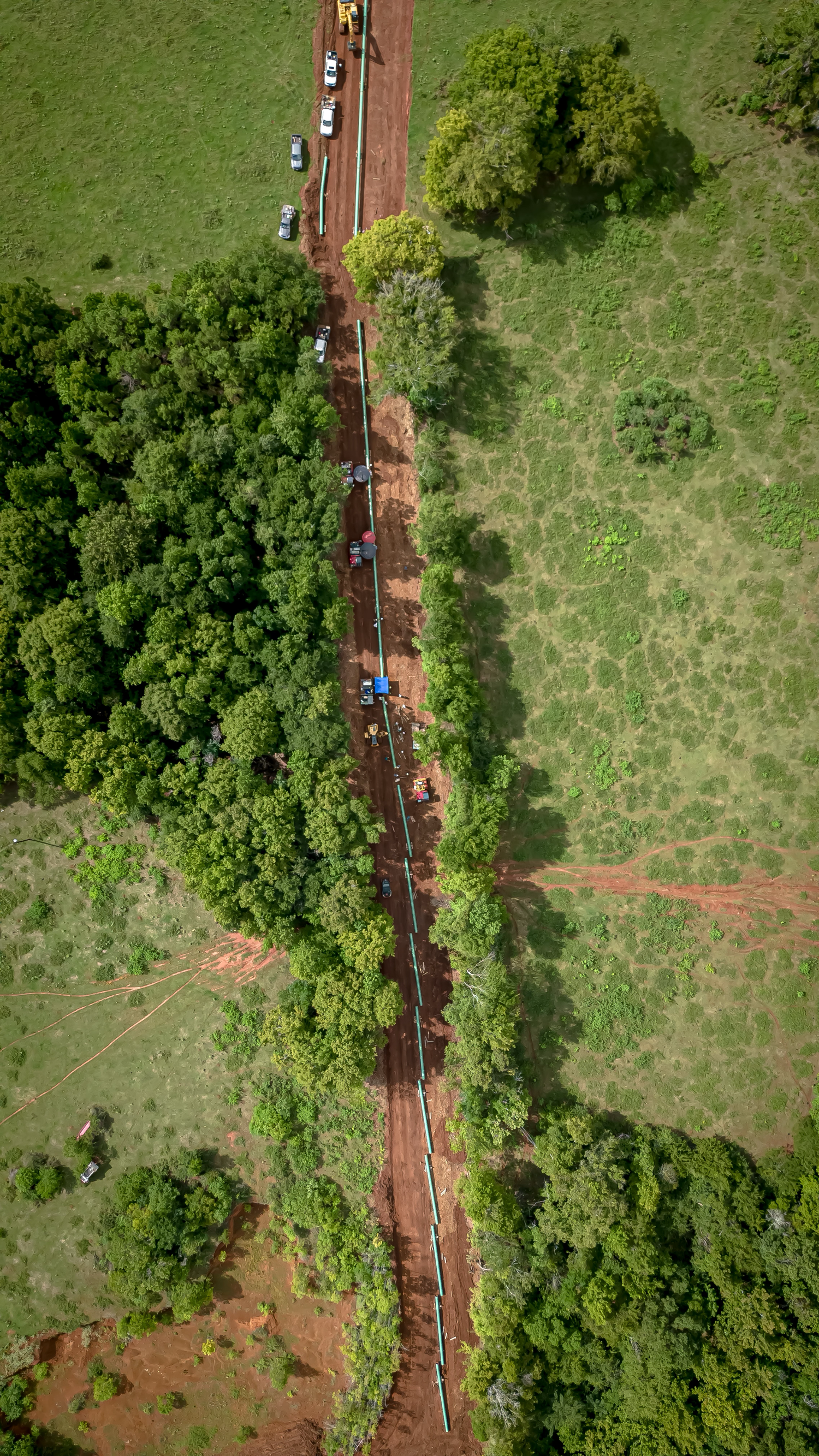 Aerial view of train tracks cutting through green fields and forest terrain.