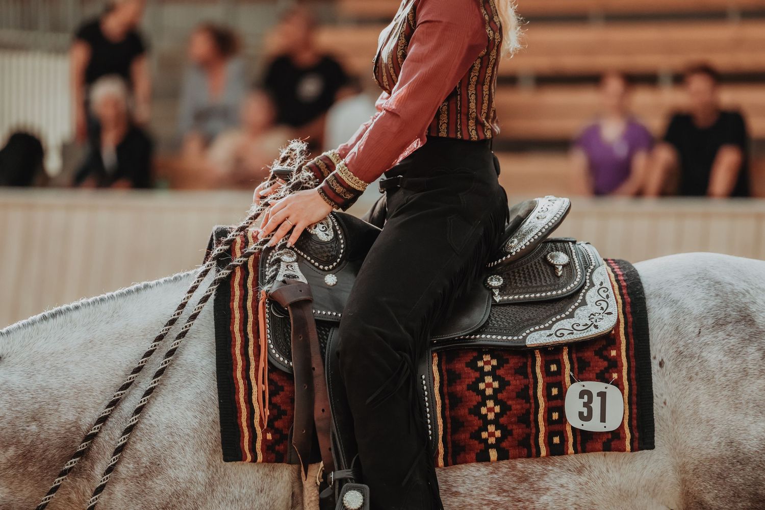 Close-up of decorative western saddle with silver details and patterned blanket on gray horse.