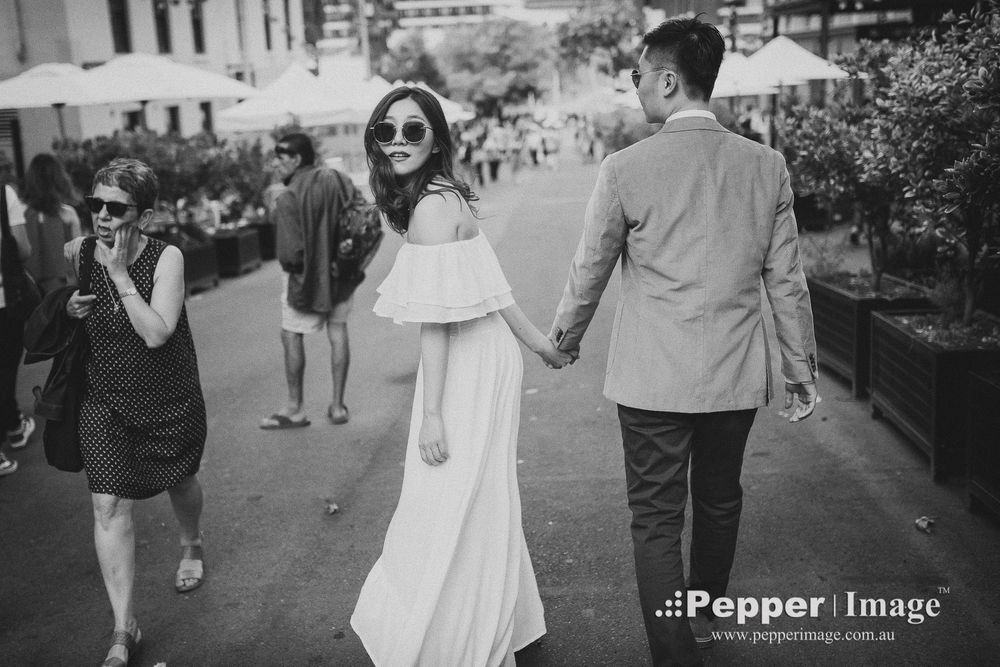 Couple holding hands walking through busy street in black and white wedding photo.