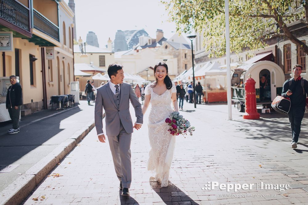 Bride and groom walk hand in hand through a sunny historic street on their wedding day.
