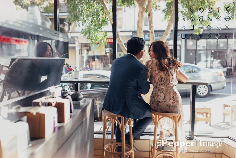 Couple sitting together at cafe window counter during romantic engagement photo session.