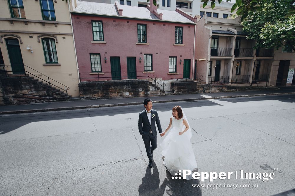 Bride and groom holding hands walking through historic Sydney street on wedding day.