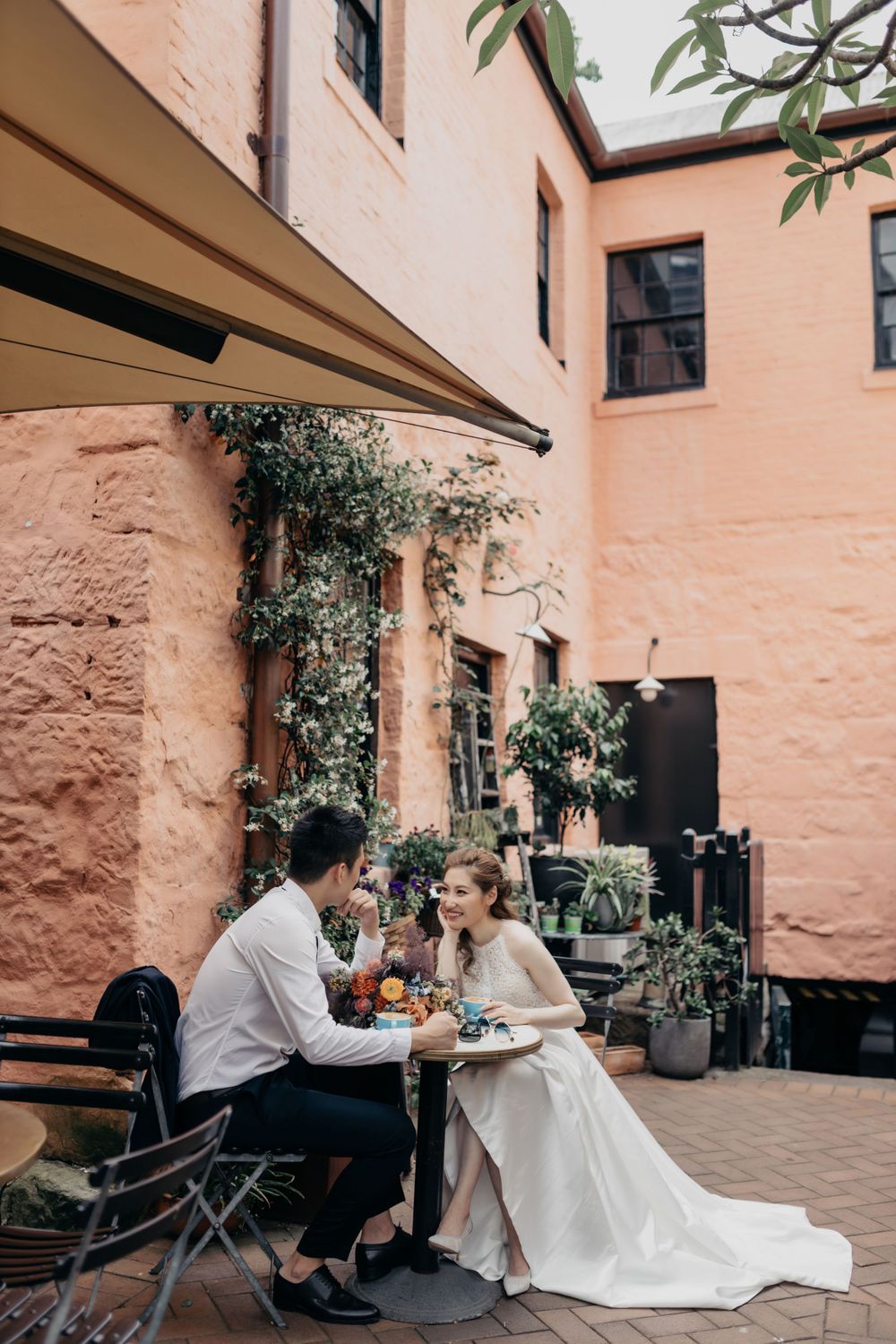 Bride and groom sitting at outdoor table in charming courtyard of historic building.