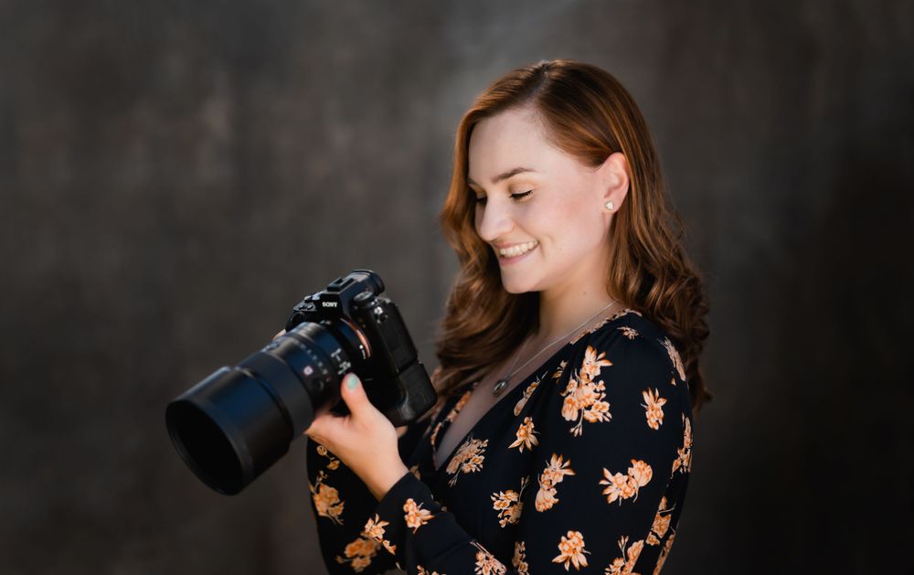 Photographer in black floral dress with camera and telephoto lens in studio setting.