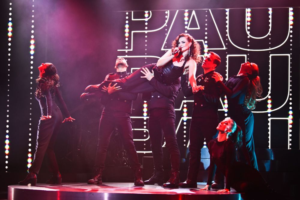 Performers dancing on stage with dramatic lighting and HAU signage in the background.