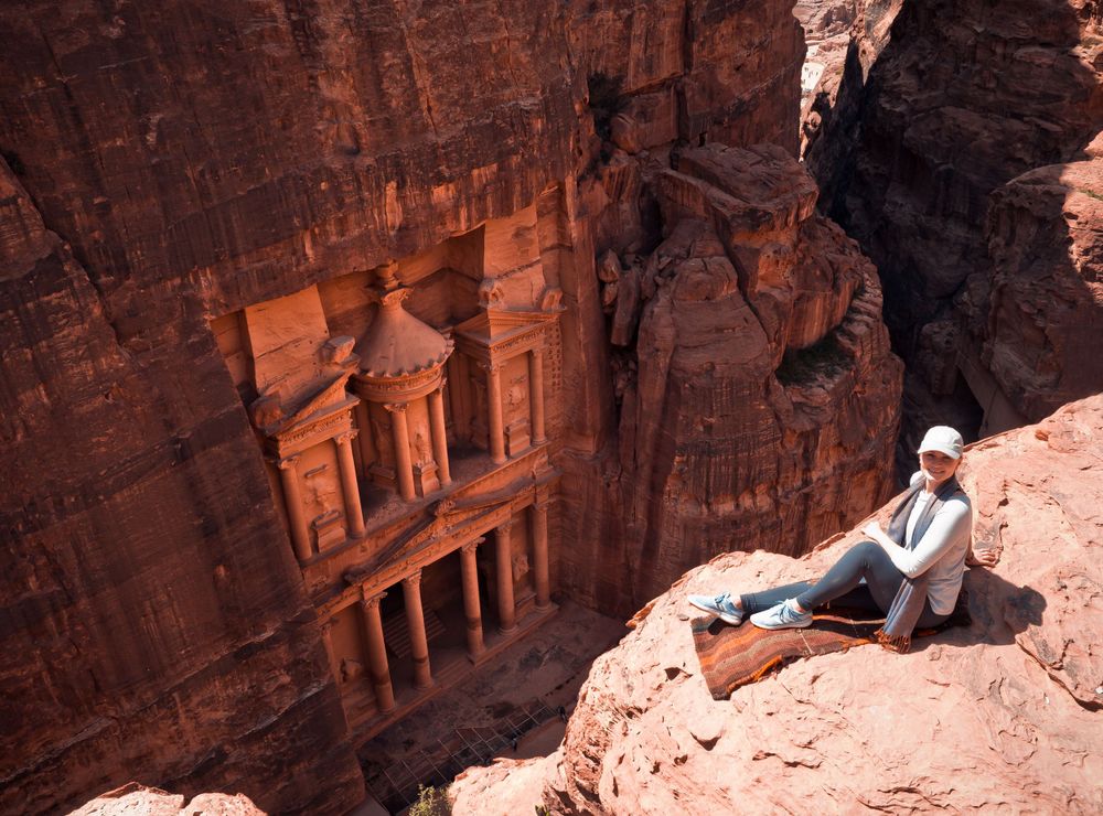 Tourist overlooking the ancient carved Treasury building at Petra in Jordan's red rock cliffs.