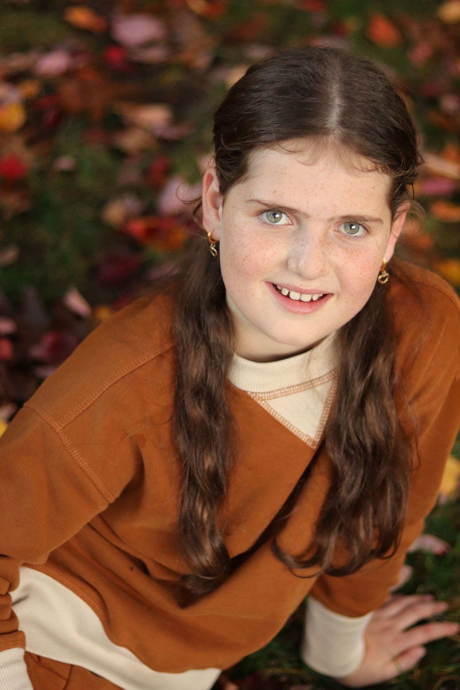 Pretty girl with bright eyes sitting in autumn leaves