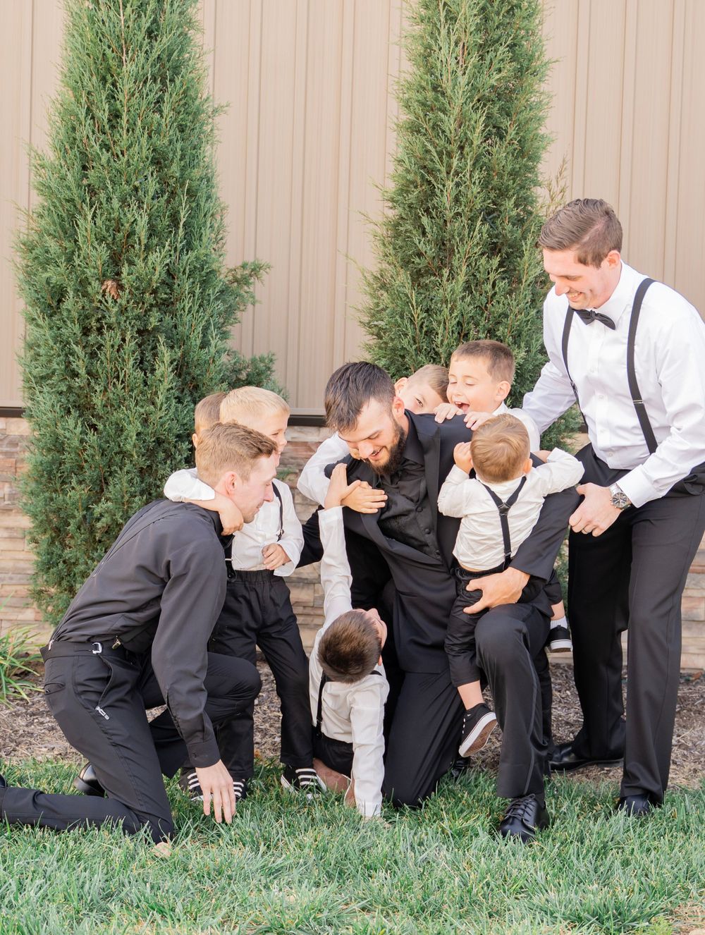 Groom in black suit playfully surrounded by young ring bearers in matching outfits on wedding day.