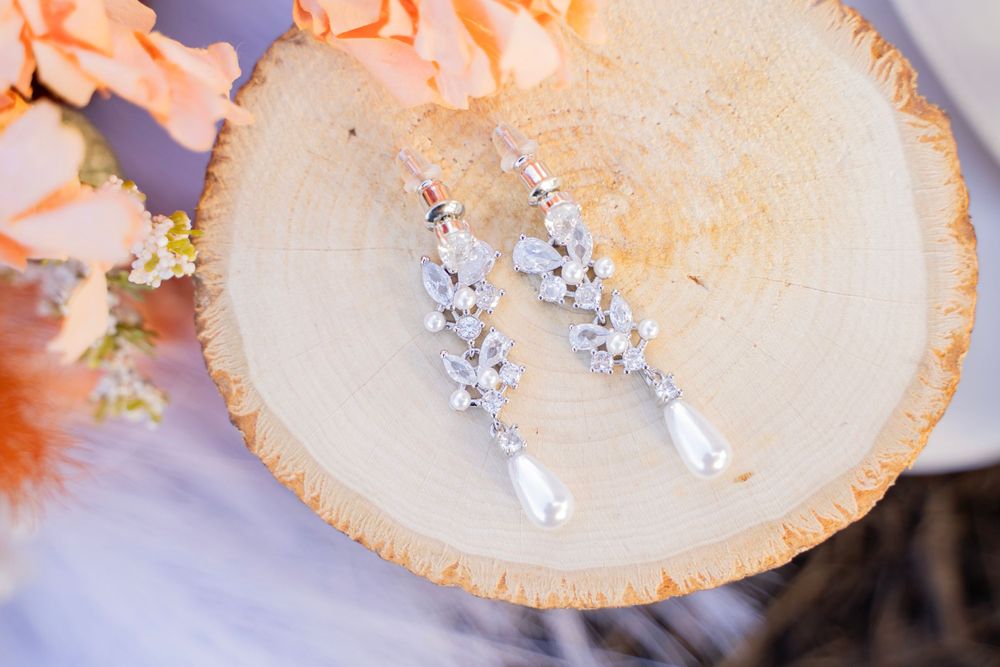 Elegant crystal and pearl drop earrings displayed on a natural wood slice with floral accents.