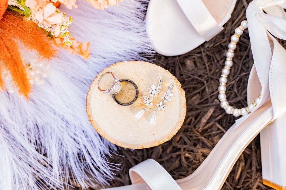 Wedding rings, pearl bracelet, and bridal accessories arranged on a rustic wood slice display.