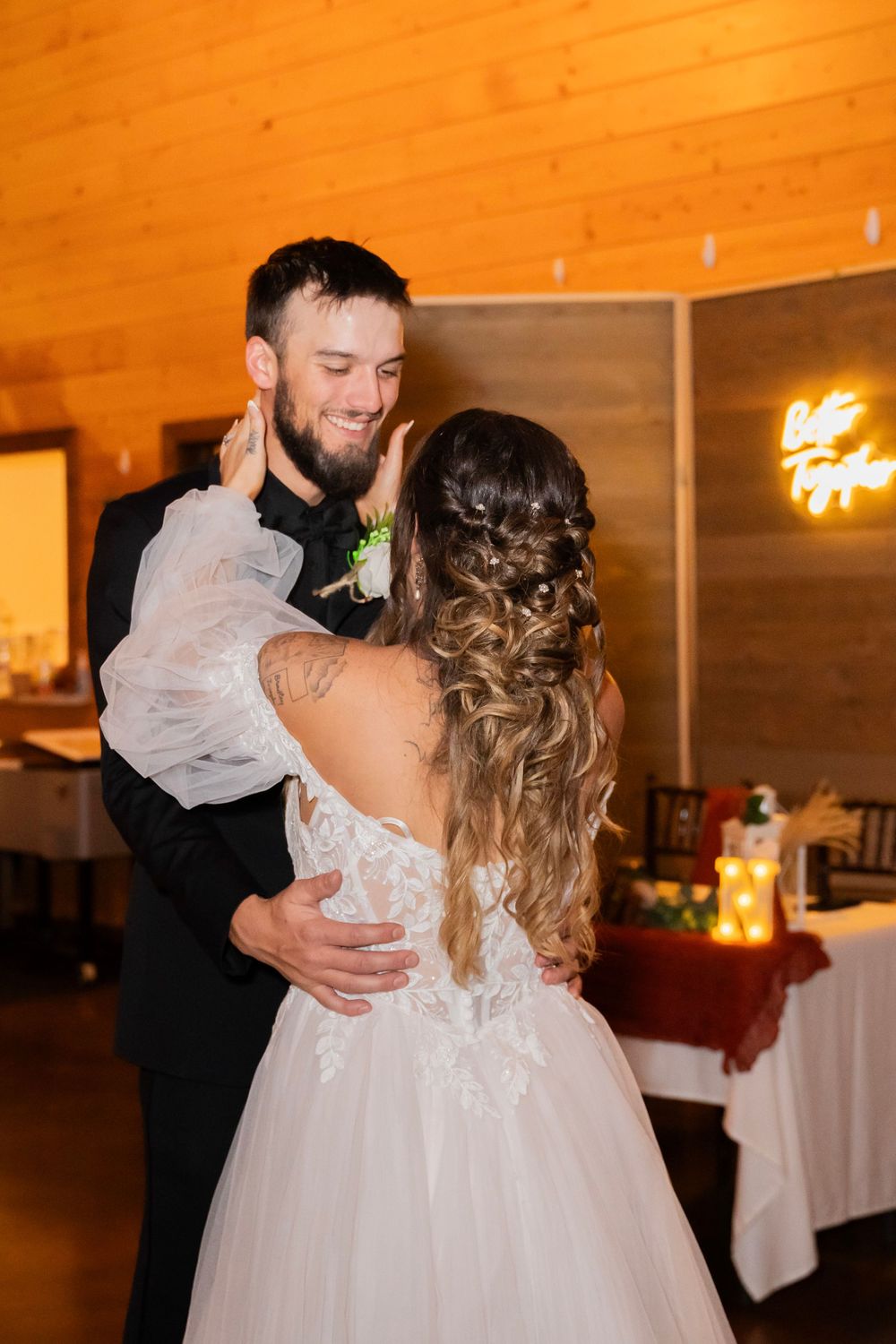 Smiling groom holds bride close during first dance at elegant rustic barn wedding reception.