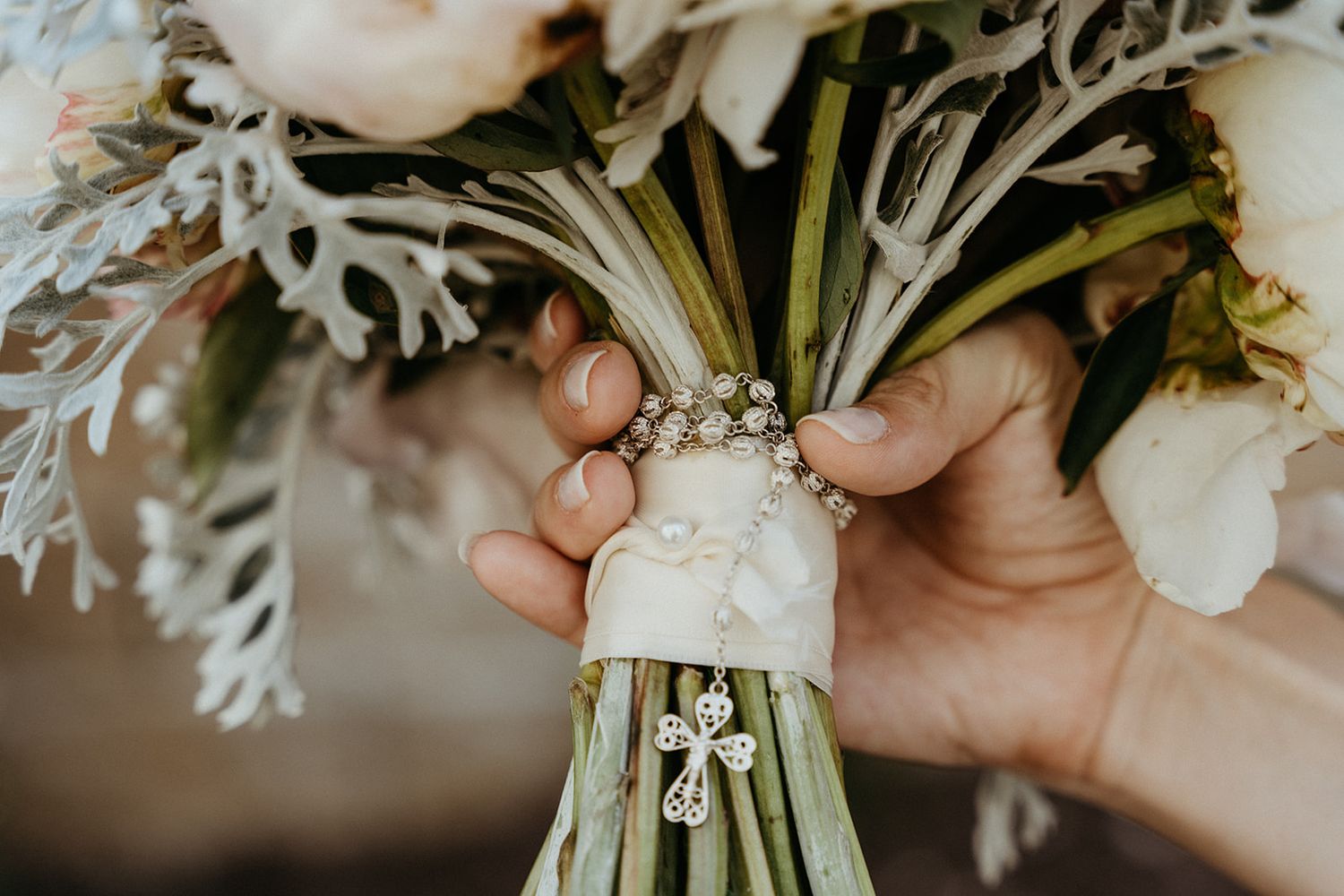 Close up of light-colored bridal bouquet with chain and cross wrapped around stems