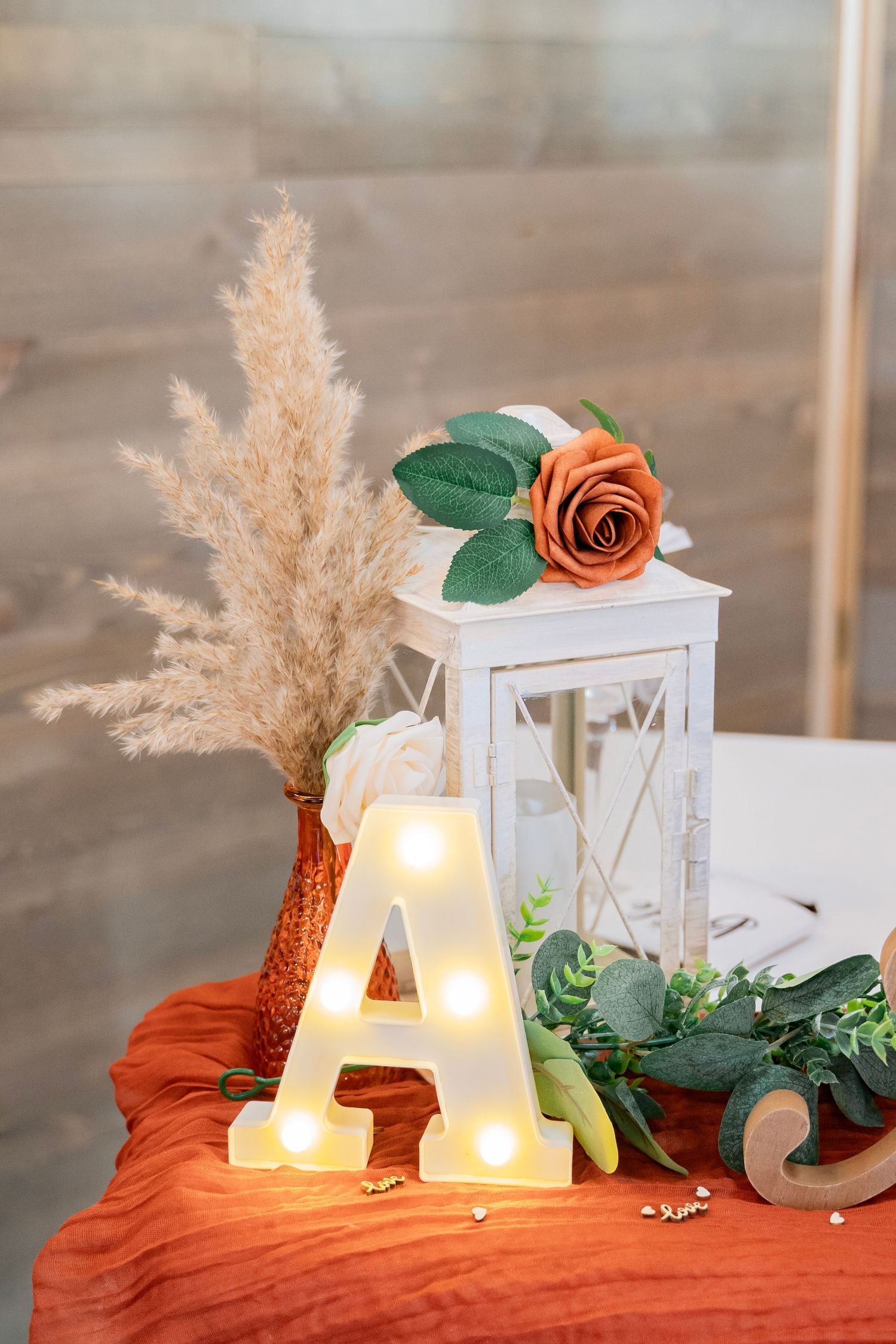 Wedding sweetheart table decor featuring a glowing letter A, white lantern, and burnt orange rose.