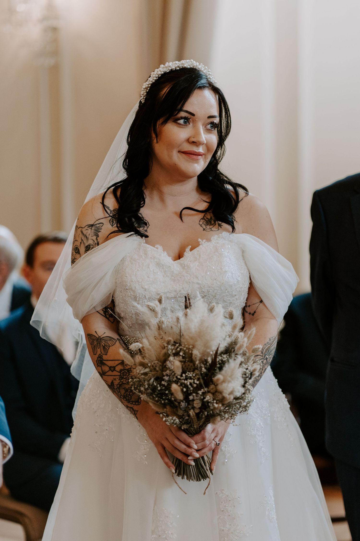a bride standing at the top of the aisle holding a dried flower bouquet.