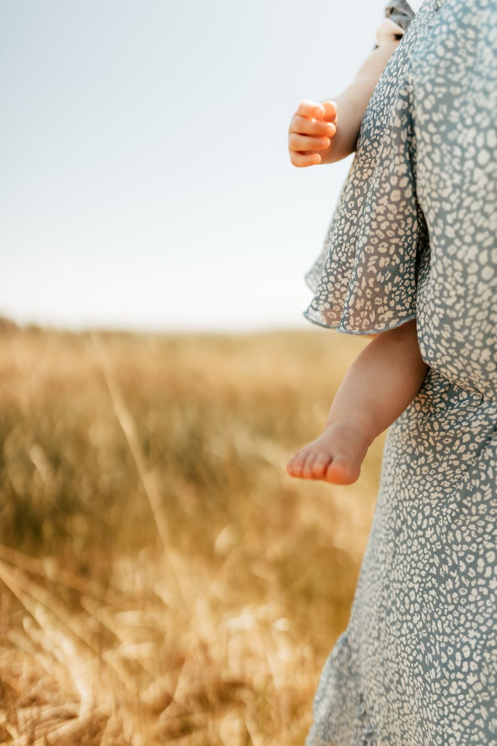 Detail shot of floral dress and bare feet walking through tall golden grass in sunlight.