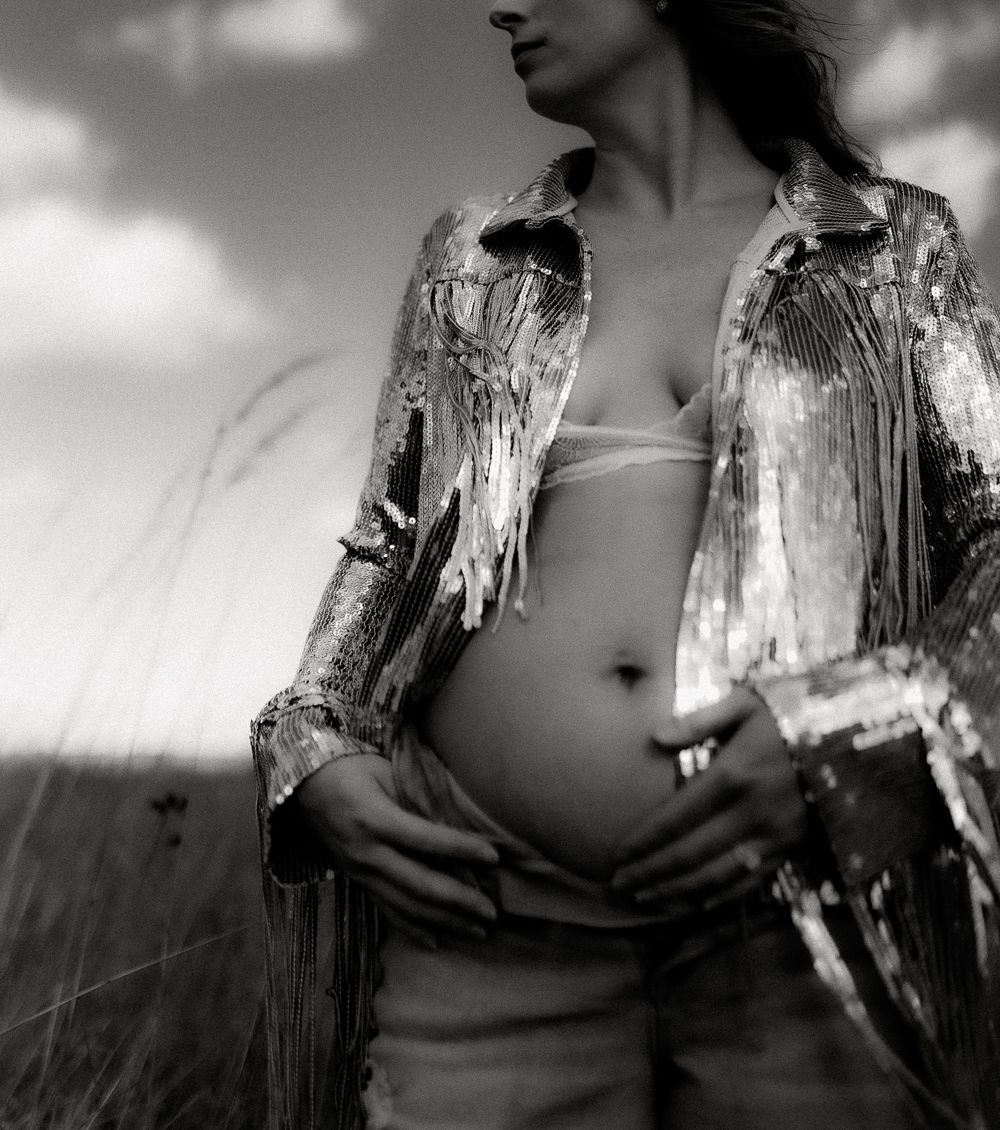 Artistic black and white portrait showing sparkly jacket and bare midriff against cloudy sky.