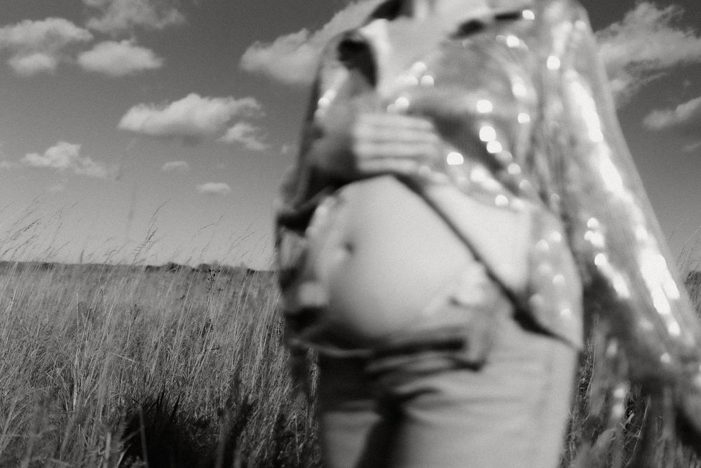 Black and white maternity photo showing a pregnant belly in a rustic field setting.