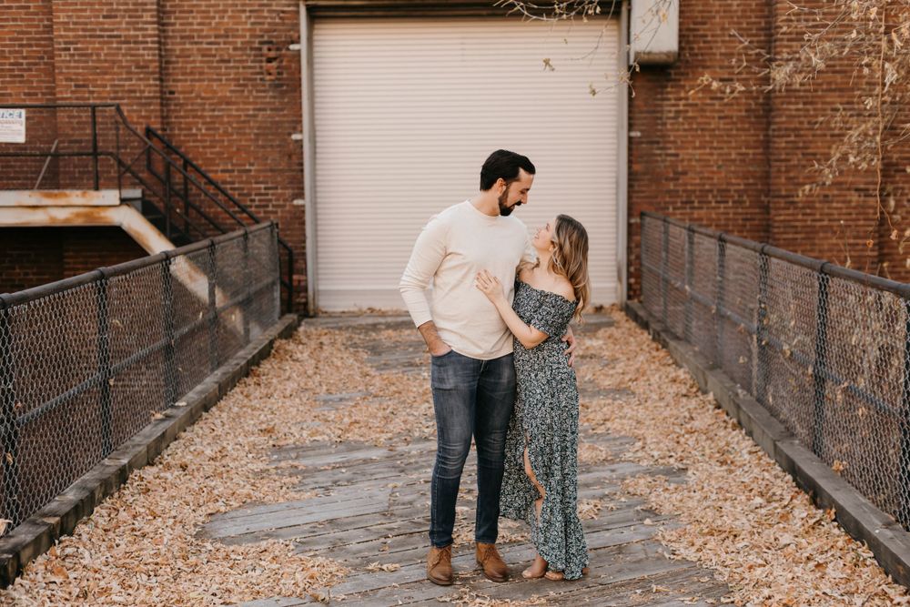 Couple gazing lovingly at each other in a sunlit brick alley during engagement session.